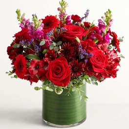 Red roses and mixed red flowers in a green glass vase