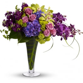 Mixed bouquet of purple, pink, and yellow flowers in a tall glass vase