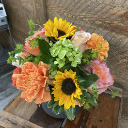 Bouquet of sunflowers, peach roses, and orange dahlias in a dark vase