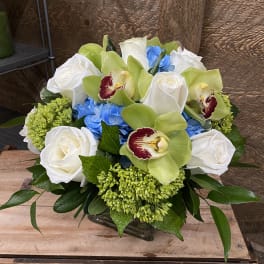 Bouquet of white roses, green orchids, and blue hydrangeas in a glass vase