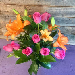 Arrangement of orange lilies and bright pink roses in a clear glass vase