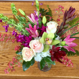 Mixed bouquet of roses, orchids, and lilies in a glass vase