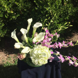 White calla lilies and pink orchids in a low vase with a pale hydrangea bloom