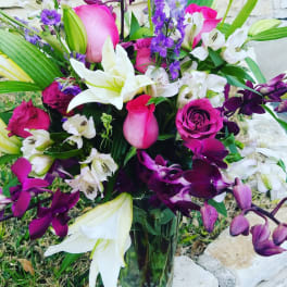 Bouquet of pink roses, white lilies, and purple orchids in a glass vase