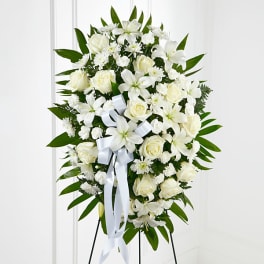 White floral standing spray with roses and lilies on a white ribboned easel