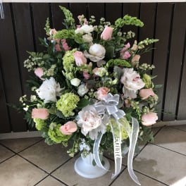 Large pink and white floral arrangement in a white pedestal vase with ribbon