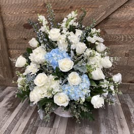 Large white floral arrangement with blue hydrangeas in a low container