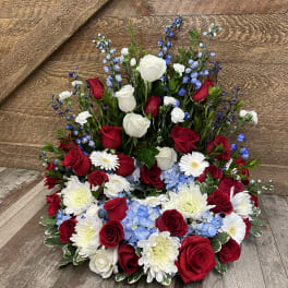 Red and white roses with blue flowers and white daisies in a low arrangement
