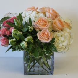 Bouquet of peach and pink roses with white hydrangeas in a square glass vase
