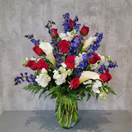 Tall bouquet of red roses, white calla lilies, and blue flowers in a glass vase