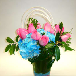 Pink roses and blue hydrangeas in a clear vase with arched handles