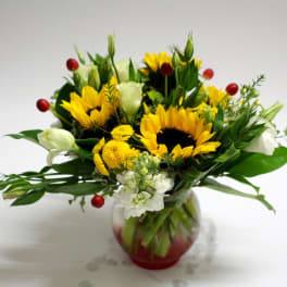 Bouquet of sunflowers, white blooms, and red berries in a glass vase