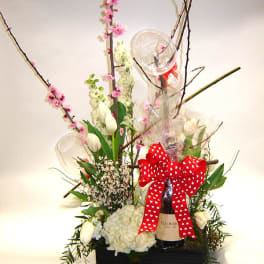 Tall floral gift arrangement with white blooms, pink blossoms, and a red bow on a bottle