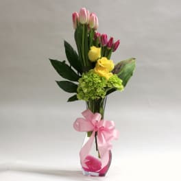 Pink and yellow tulips with green hydrangea in a glass vase with a pink ribbon