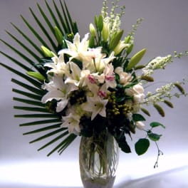 White lilies and orchids arranged in a clear glass vase