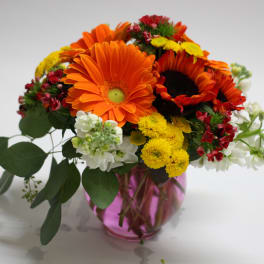 Bouquet of orange gerbera daisies and yellow flowers in a pink glass vase