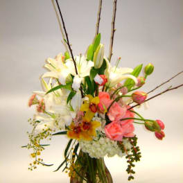 Tall mixed floral arrangement in a glass vase with lilies and pink roses