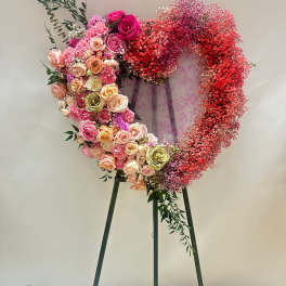 Heart-shaped floral wreath on a stand with pink and red roses