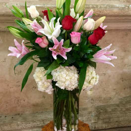 Tall bouquet of pink and red roses with lilies in a glass vase