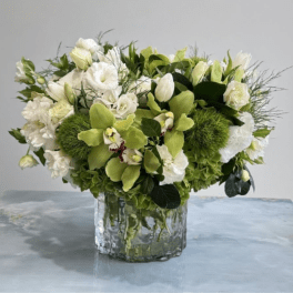Low arrangement of white blooms and green orchids in a clear glass vase