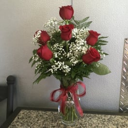 Tall arrangement of red roses and white filler flowers in a clear vase with a red bow