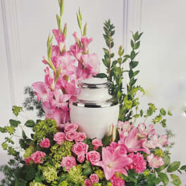 Pink floral arrangement around a white urn with silver trim