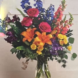 Colorful bouquet with roses, lilies, and tall blue and pink spikes in a glass vase