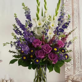 Purple roses and white gladiolus in a clear glass vase