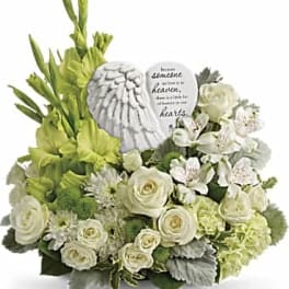 White and green sympathy arrangement with roses and gladiolus around an angel wing keepsake.