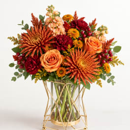 Orange and red floral arrangement in a glass vase with gold stand