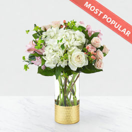 Bouquet of white and pink flowers in a clear glass vase with a gold base