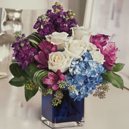 Bouquet of white roses, blue hydrangea, and purple flowers in a blue glass vase