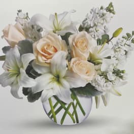 Cream roses and white lilies in a round glass vase