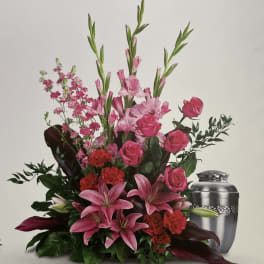 Pink lilies and roses arranged with red carnations beside a silver urn.