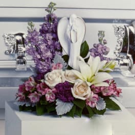 Purple and pink floral arrangement with white lilies and roses in a silver casket