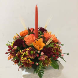 Orange and burgundy floral arrangement with a tall red candle