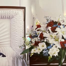 Casket spray with red roses, white lilies, and blue flowers beside a folded flag