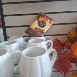 White ceramic mugs displayed with a pumpkin spice sign and autumn leaves.