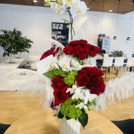 Tall arrangement of red roses and white orchids in a white vase