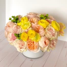 Round bouquet of pale pink and yellow flowers in a white box