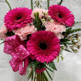 Pink gerbera and carnations in a glass vase with a polka-dot ribbon