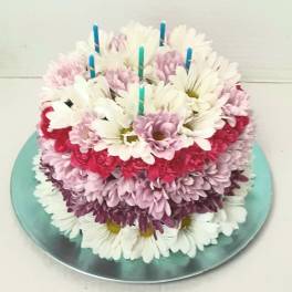 Round cake covered with white, pink, and purple daisies and candles on top