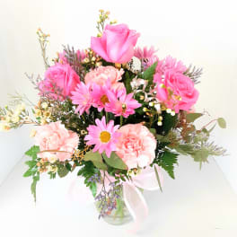 Pink roses and daisies in a clear glass vase with a ribbon