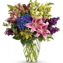 Mixed bouquet with pink lilies, blue hydrangea, and purple flowers in a clear vase