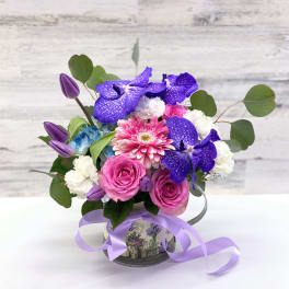 Pink and purple mixed bouquet in a decorative tin container with ribbon