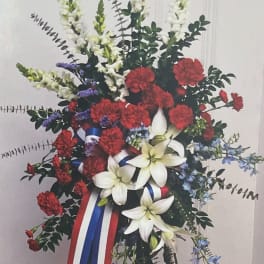 Standing floral spray with red carnations, white lilies, and blue accents