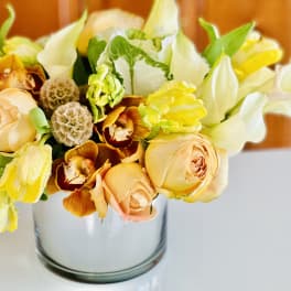 Bouquet of peach roses, yellow blooms, and white flowers in a glass vase