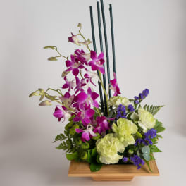 Purple orchids and pale carnations in a wooden container
