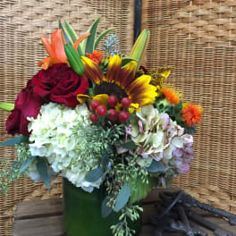 Mixed bouquet with roses, hydrangeas, and a sunflower in a green vase