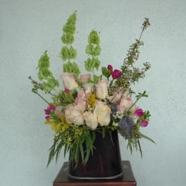 Mixed bouquet of pale roses and green snapdragons in a dark vase